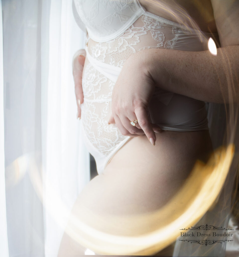 A bridal boudoir portrait of a woman in blue lingerie against a dreamy pink and purple cloud backdrop, looking down as her hair falls over her shoulder, representing boudoir portraits in Flint MI