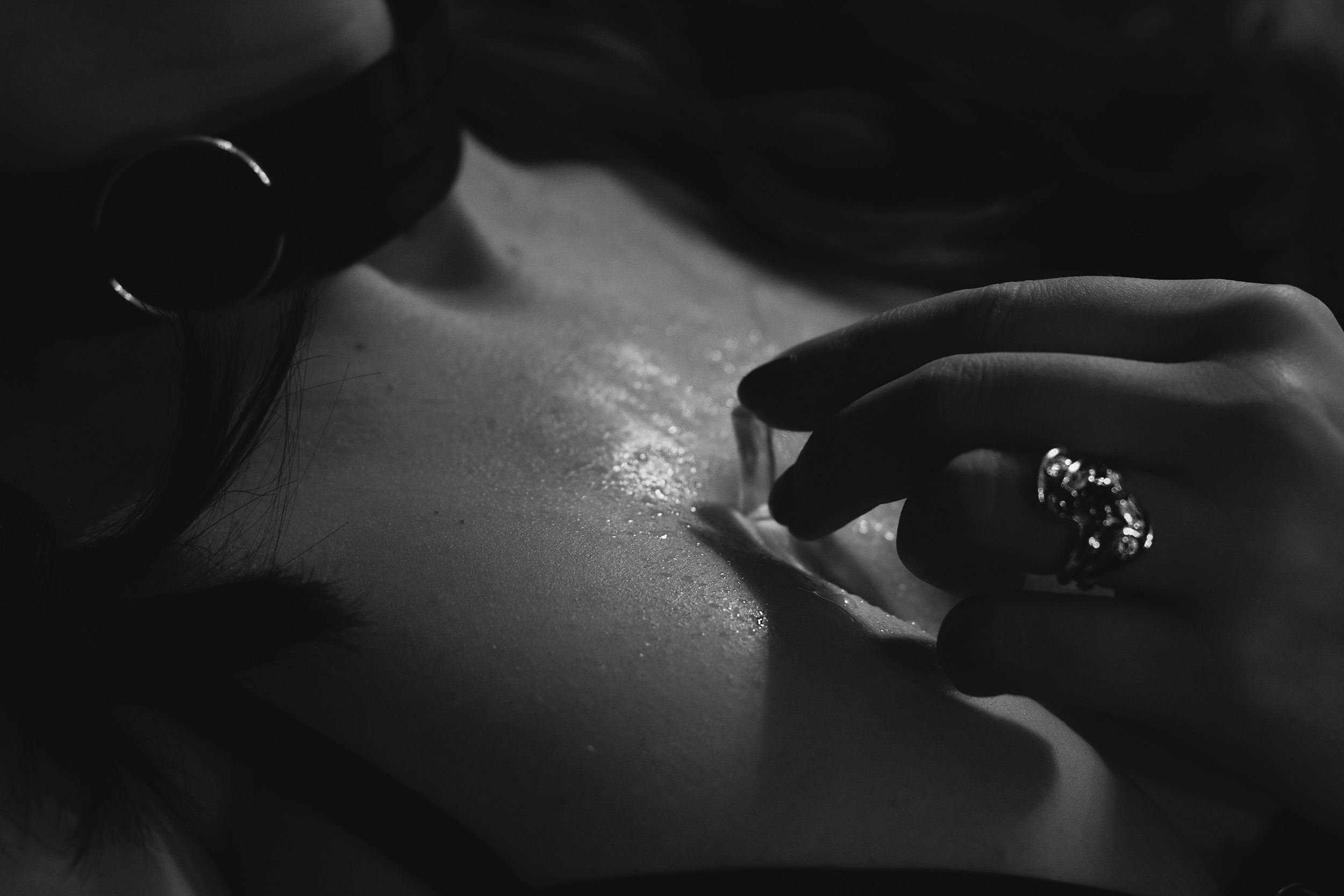 A black and white close up photo of a woman holding a melting ice cube on chest wearing a vintage wedding ring