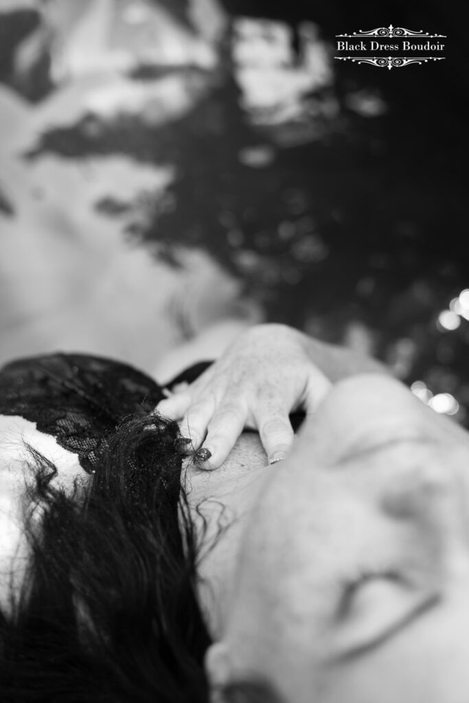 A black and white detail boudoir photograph of a woman lying back with closed eyes, wearing lace. Fingers rest gently on her chest, creating a serene, relaxed mood in Mid-Michigan.